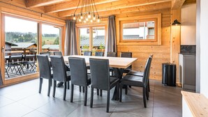 Un comedor con mesa y sillas de madera, ventanas amplias y vistas al exterior.
