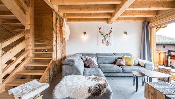 Un interior de madera con una escalera, un sofá gris y una alfombra mullida.