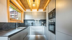Una cocina moderna con electrodomésticos de acero inoxidable, vigas de techo de madera y una ventana con vista a un edificio.