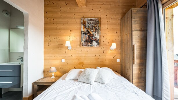 Ein Schlafzimmer mit Holzboden, einem Bett mit weißer Bettwäsche, zwei Nachttischlampen, einem Bild an der Wand und einem Fenster mit Vorhängen.