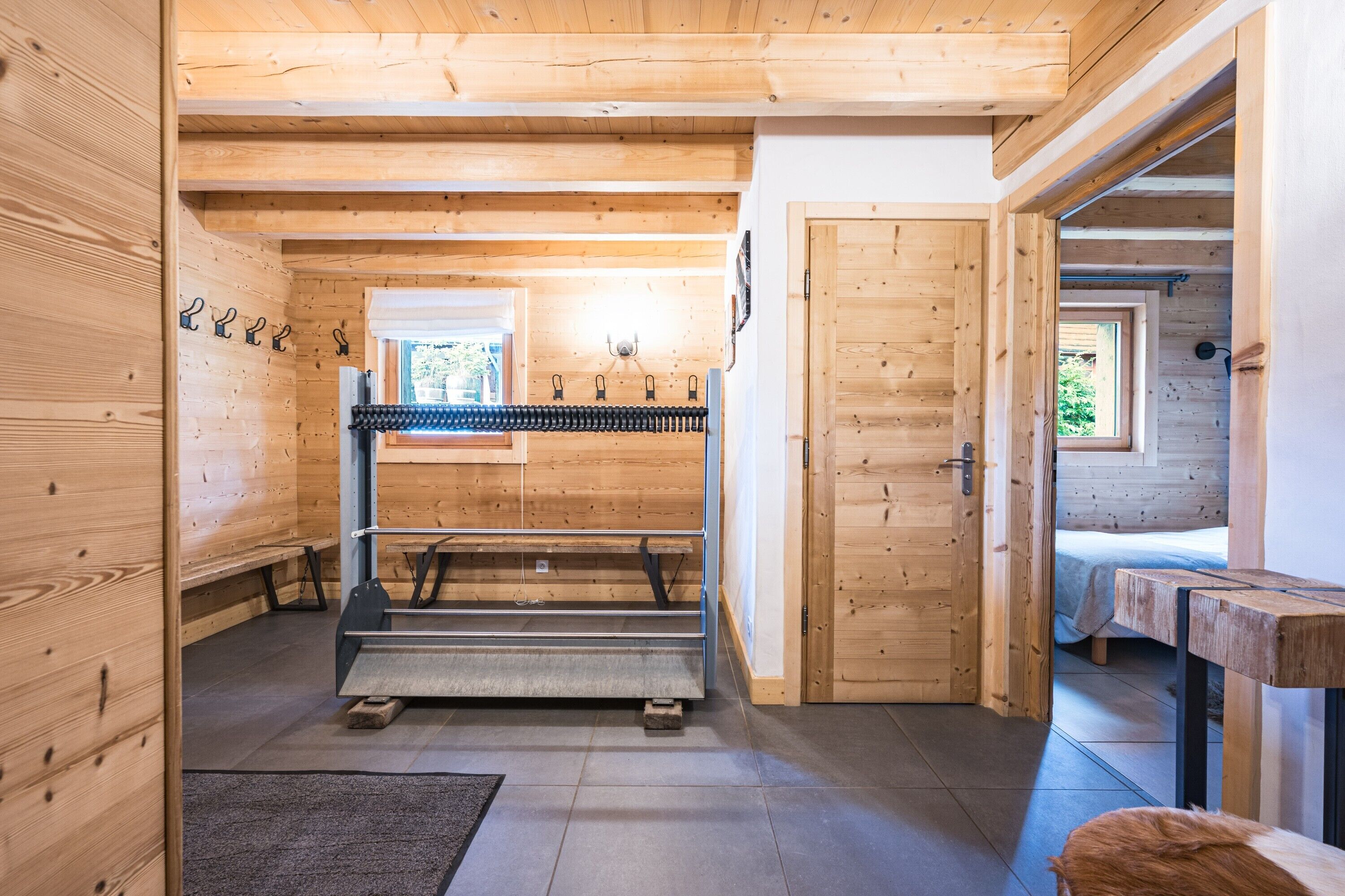A wooden interior with a bed, a bench, and a rack with hooks.