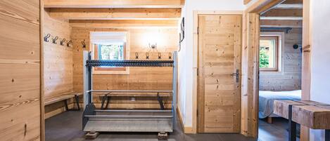A wooden interior with a bed, a bench, and a rack with hooks.