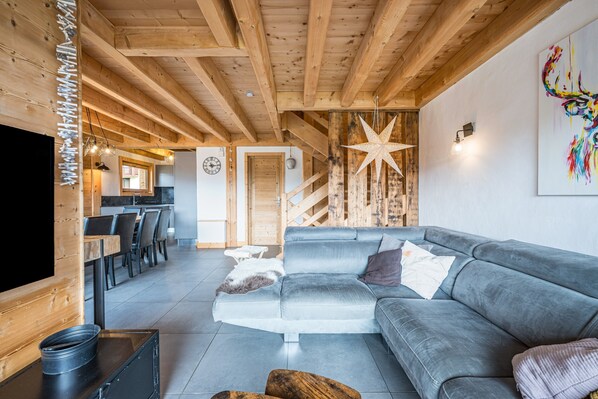 A modern interior with a grey sofa, wooden ceiling beams, a star decoration, and a flat-screen TV.