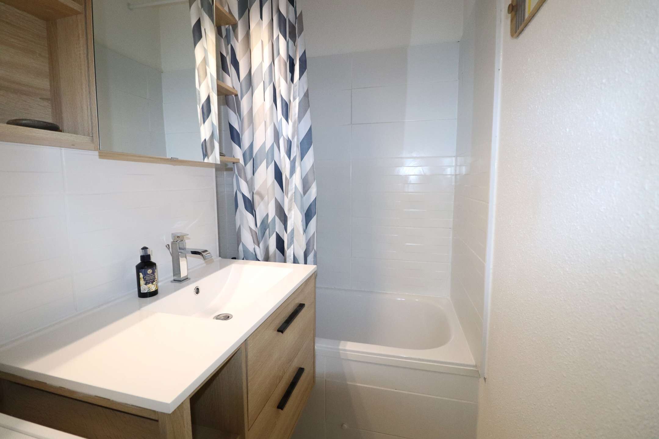 A modern bathroom with a white sink, wooden vanity, and a shower area.