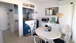 A compact kitchen with a microwave, a sink, and a refrigerator. There is a dining area with a white table and chairs. - Spacious 3 room air-conditioned apartment terrace garage (LE GRAU DU ROI)