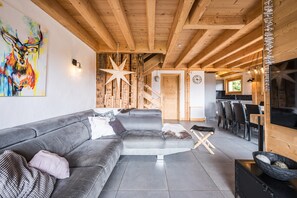 Un soggiorno moderno con un divano angolare grigio, un soffitto in legno e una scala che conduce a un piano superiore.