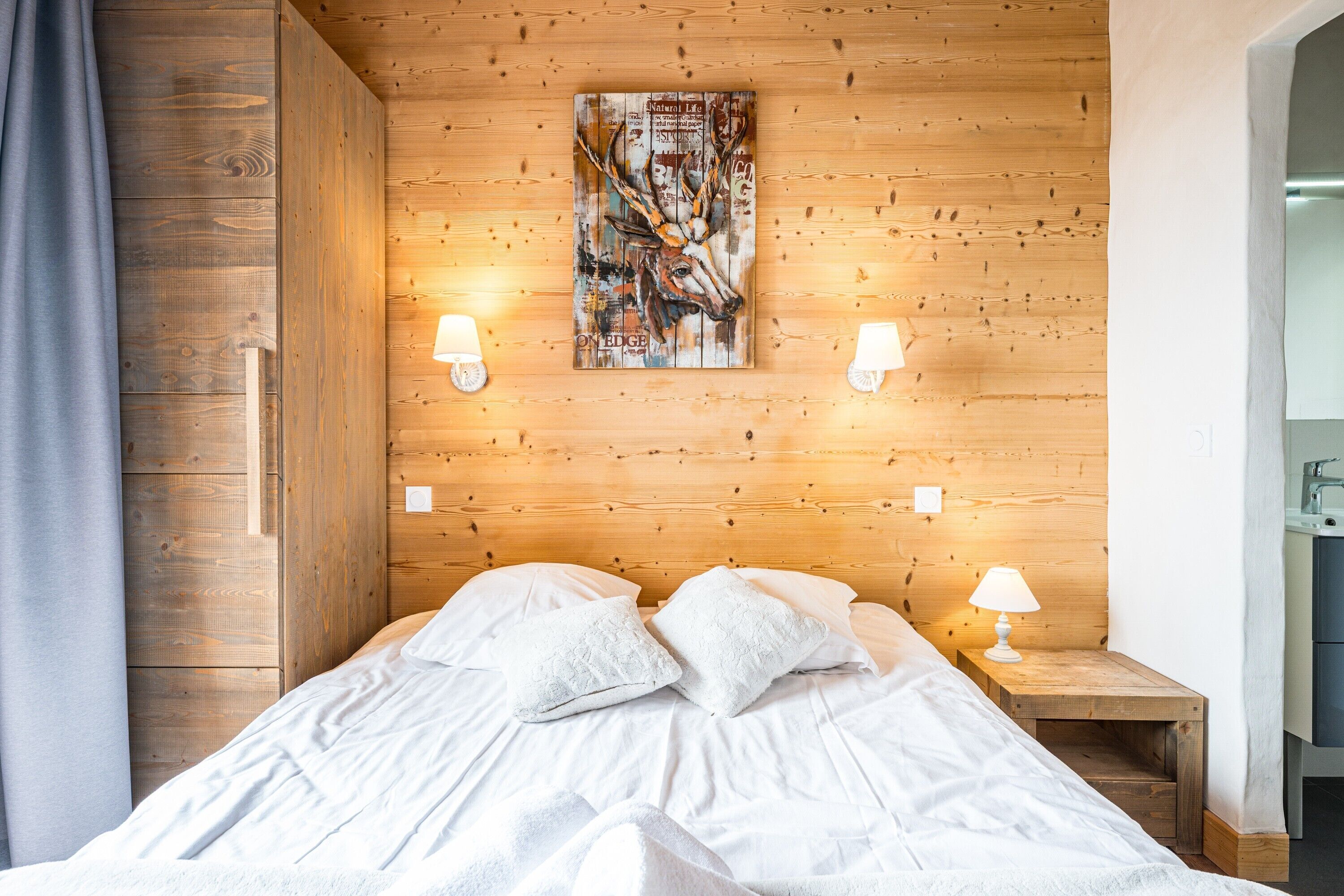 A wooden-paneled room with a bed, two bedside lamps, and a wall-mounted artwork.