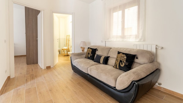 A living room with a sofa, a window with curtains, a door, and a hallway leading to another room.