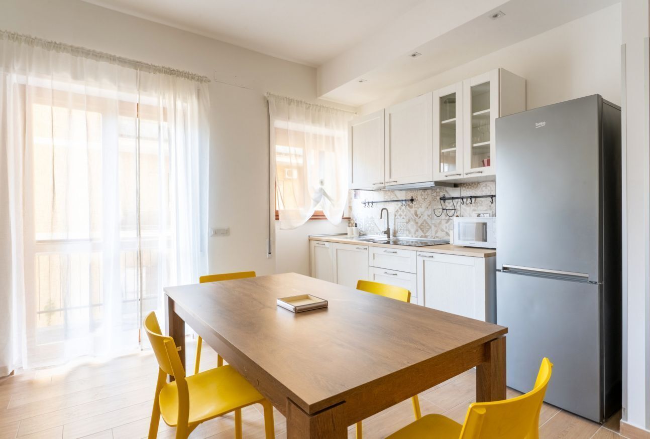 Una cucina moderna con mobili bianchi, un frigorifero in acciaio inossidabile e un tavolo da pranzo con sedie gialle.
