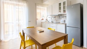 A modern kitchen with white cabinets, a stainless steel refrigerator, and a dining table with yellow chairs.