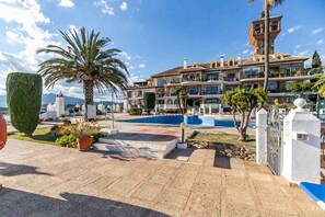 A hotel with a swimming pool, a large palm tree, and a mountain view. - Apartment 'Golf Course View' with Mountain View, Wi-Fi and Air Conditioning (Las Lagunas de Mijas)