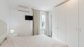 A bedroom with a bed, a TV, a window with curtains, and a wardrobe.