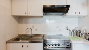 A kitchen with white cabinets, a stainless steel sink, a stove, and a range hood.