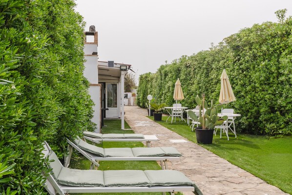 A pathway leading to a building with a covered area, surrounded by greenery and outdoor seating.