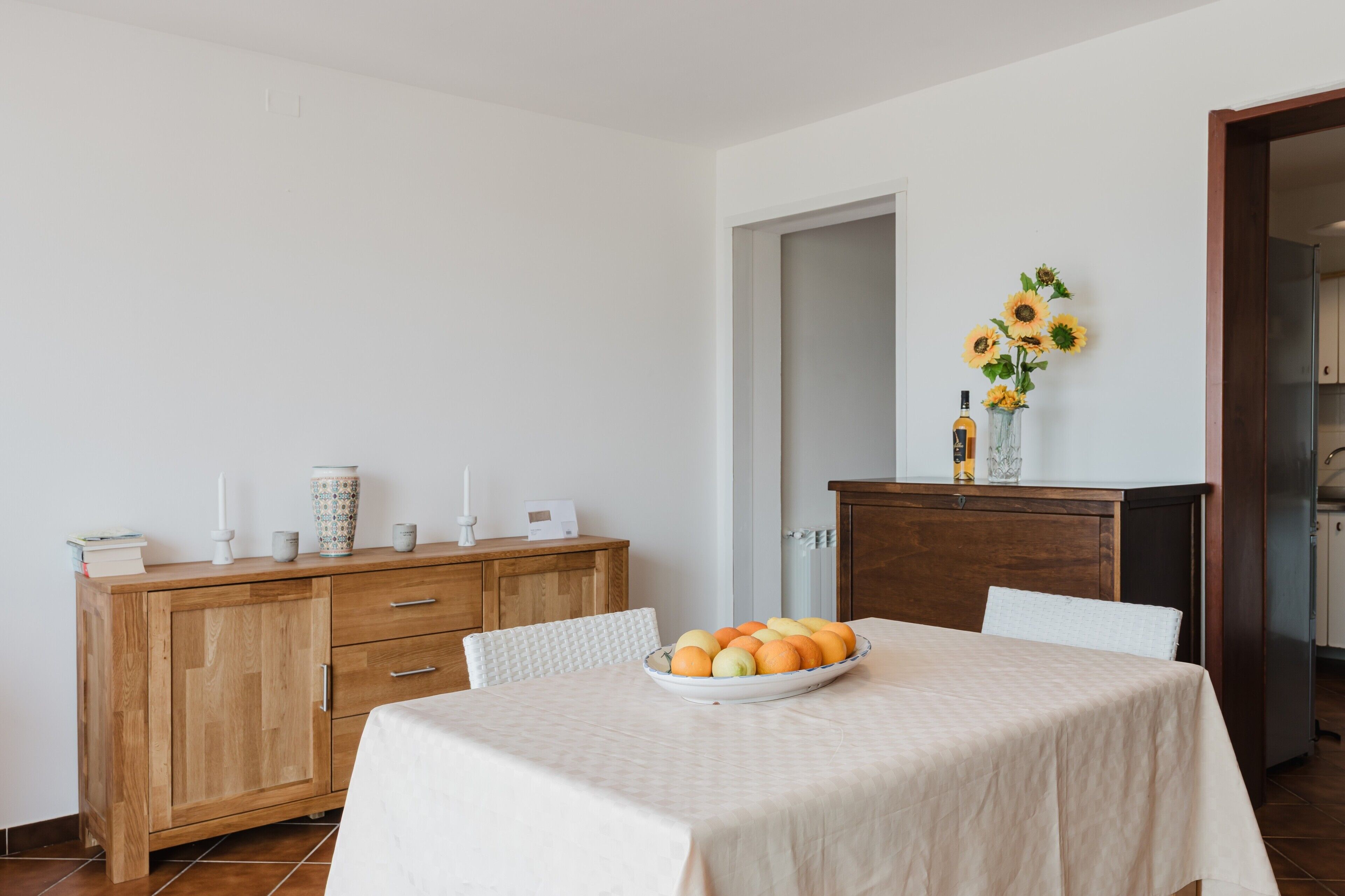 Ein Essbereich mit einem Tisch für zwei Personen, einem Holzschrank und einer Vase mit Sonnenblumen an der Wand.