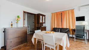 A dining area with a table set for two, a cabinet, a television, and a window with curtains.