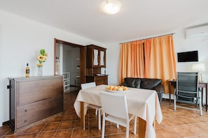 A dining area with a table set for two, a cabinet, a television, and a window with curtains.