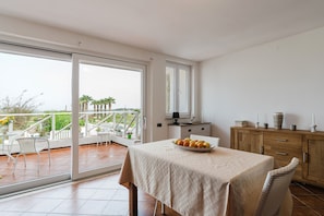 Een balkon met een eettafel, stoelen en uitzicht op palmbomen en de zee.