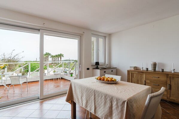 A balcony with a dining table, chairs, and a view of palm trees and the sea.