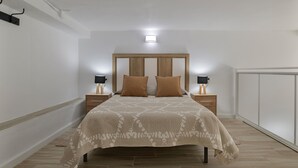 A bedroom with a bed, two bedside tables, a nightstand, a headboard, and a wall-mounted light fixture.