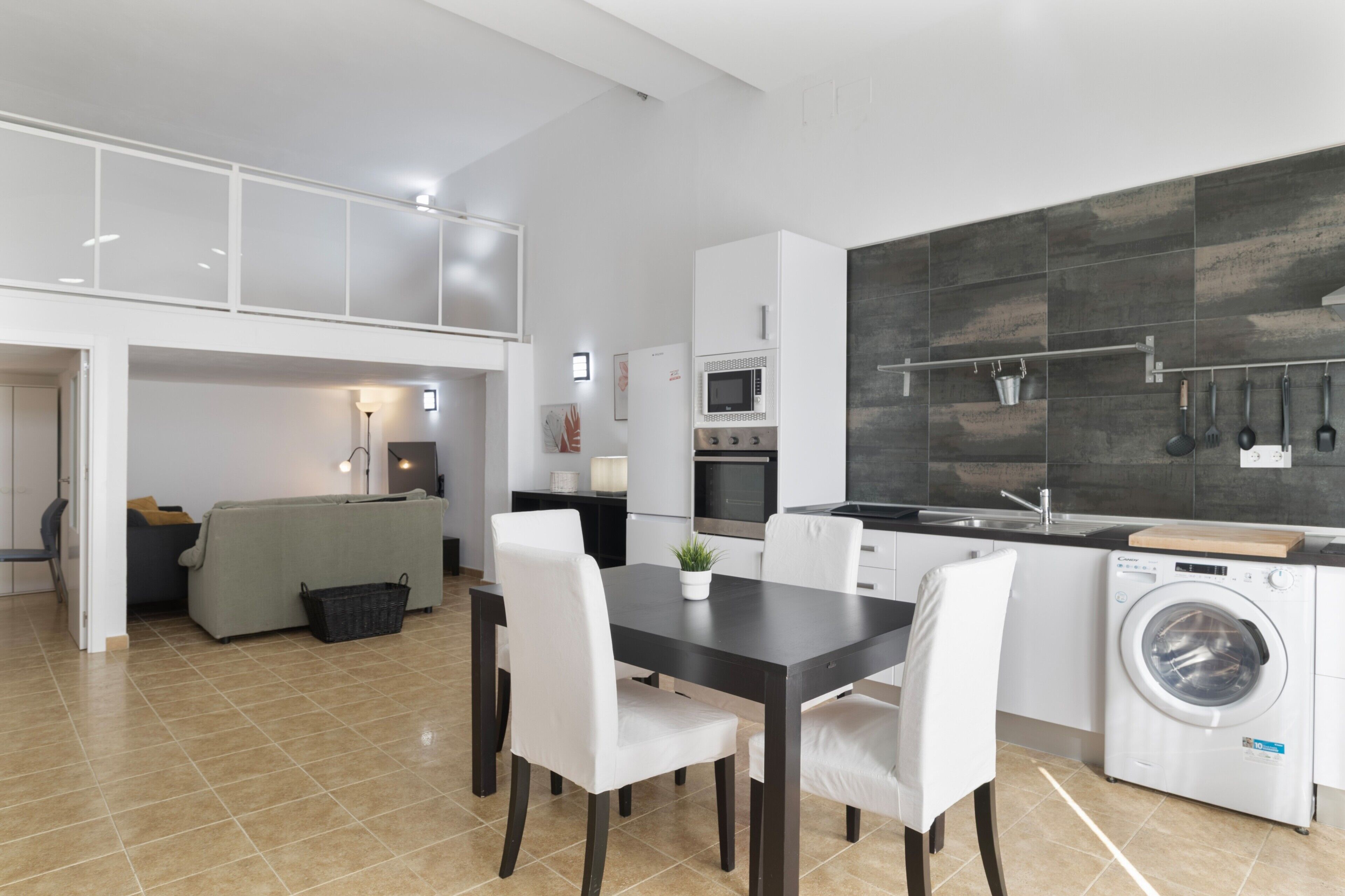 Una cocina moderna con lavadora, un comedor con mesa y sillas, y una sala de estar con sofá y lámpara.