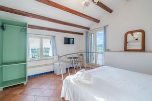 A bedroom with a bed, a green wardrobe, a television, a window with curtains, and a view of the outdoors.
