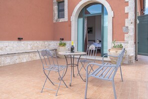 An outdoor patio with metal chairs and a table, a bottle of wine, and potted plants.