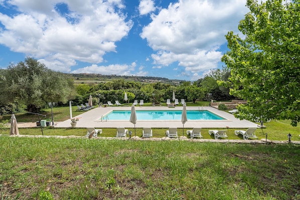 A rectangular pool with lounge chairs and umbrellas, surrounded by grass and trees. - Room 'Cabernet R12' with Shared Pool, Wi-Fi and Air Conditioning (Siracusa)