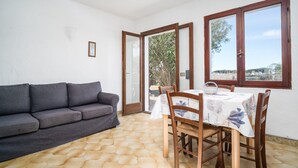 A room with a sofa, dining table, chairs, and large windows. - Apartment 'Nibaru 1 Mare' with Shared Terrace, Shared Garden and Wi-Fi (Budoni)