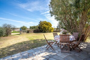 A patio with stone flooring, wooden chairs, and a table with a patterned tablecloth. - Holiday Home 'Sun Vacanze Turchese 2' with Shared Garden · Wi-Fi · A/C · Private Barbecue (Budoni)