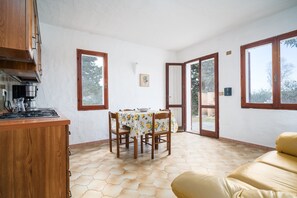 Eine Küche mit Gaskochfeld, Holzschränken, einem Esstisch mit Stühlen und großen Fenstern.