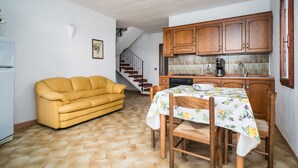 A compact living space with a sofa, dining table, wooden cabinets, and a staircase.