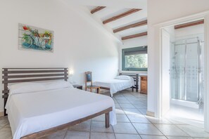 Une chambre avec deux lits, une tête de lit en bois, un tableau, une fenêtre et un espace douche.