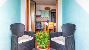 Une pièce avec deux fauteuils en osier, une plante en pot ornée de fleurs et une vue sur un coin cuisine comprenant des placards et une table à manger.
