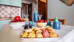 Une table de petit-déjeuner avec des viennoiseries, des fruits et une cafetière.