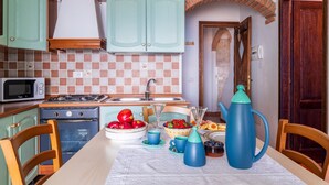 Une cuisine avec des meubles de couleur turquoise, un four à micro-ondes, une cuisinière et une table dressée avec des fruits et une théière.