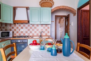 A kitchen with teal cabinets, a microwave, stove, and a table set with fruits and a teapot.