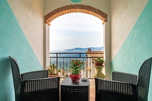 A balcony with wicker chairs, a table, and potted plants.