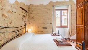 Un dormitorio con pared de piedra, una cama con cubrecama blanco, un armario de madera y una ventana con vistas.