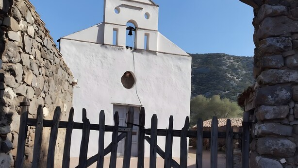 Una iglesia blanca con un campanario, una verja de madera y un muro de piedra.