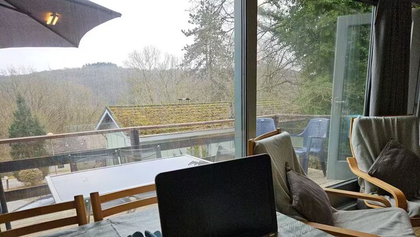 A laptop on a table with a view of a house and trees outside a window. - Nawal's Belle Vue Dinant/Givet (Hastière)