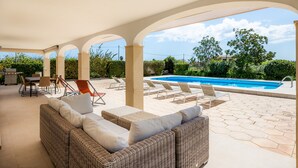 Une terrasse extérieure aménagée avec des meubles en osier, une piscine et une vue sur le paysage environnant.