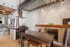Una cucina moderna con isola centrale, bicchieri da vino appesi e camino in mattoni.