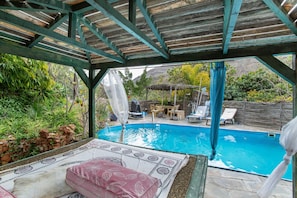 Area piscina scoperta coperta con patio, poltrone relax e tavolo.