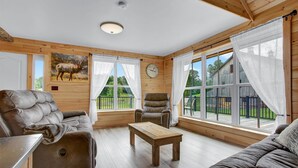A cozy room with wooden walls, a leather sofa, a wooden coffee table, and large windows with curtains.
