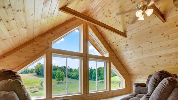 A high-ceilinged room with large windows, wooden beams, and a ceiling fan.