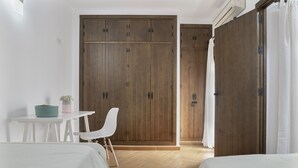 Une chambre avec deux lits, une armoire en bois, un bureau blanc avec une chaise et une petite table sur laquelle est posé un vase.