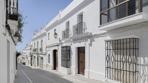 Une rue étroite bordée de bâtiments blancs, avec des balcons dotés de garde-corps en métal et des fenêtres équipées de volets.