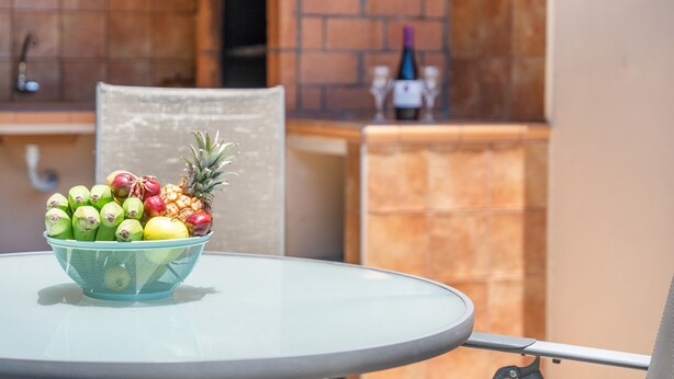 Una mesa con un frutero que contiene manzanas, plátanos y una piña.