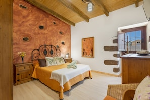 Une chambre à coucher avec une tête de lit en bois, un lit recouvert d’une couvre-lit blanche et jaune, une table de chevet ornée d’un vase de fleurs et une commode en bois avec un miroir.